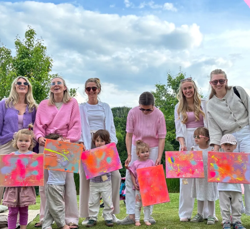 Kinder halten stolz ihre selbst gemalten Leinwände in die Kamera, dahinter ihre Eltern